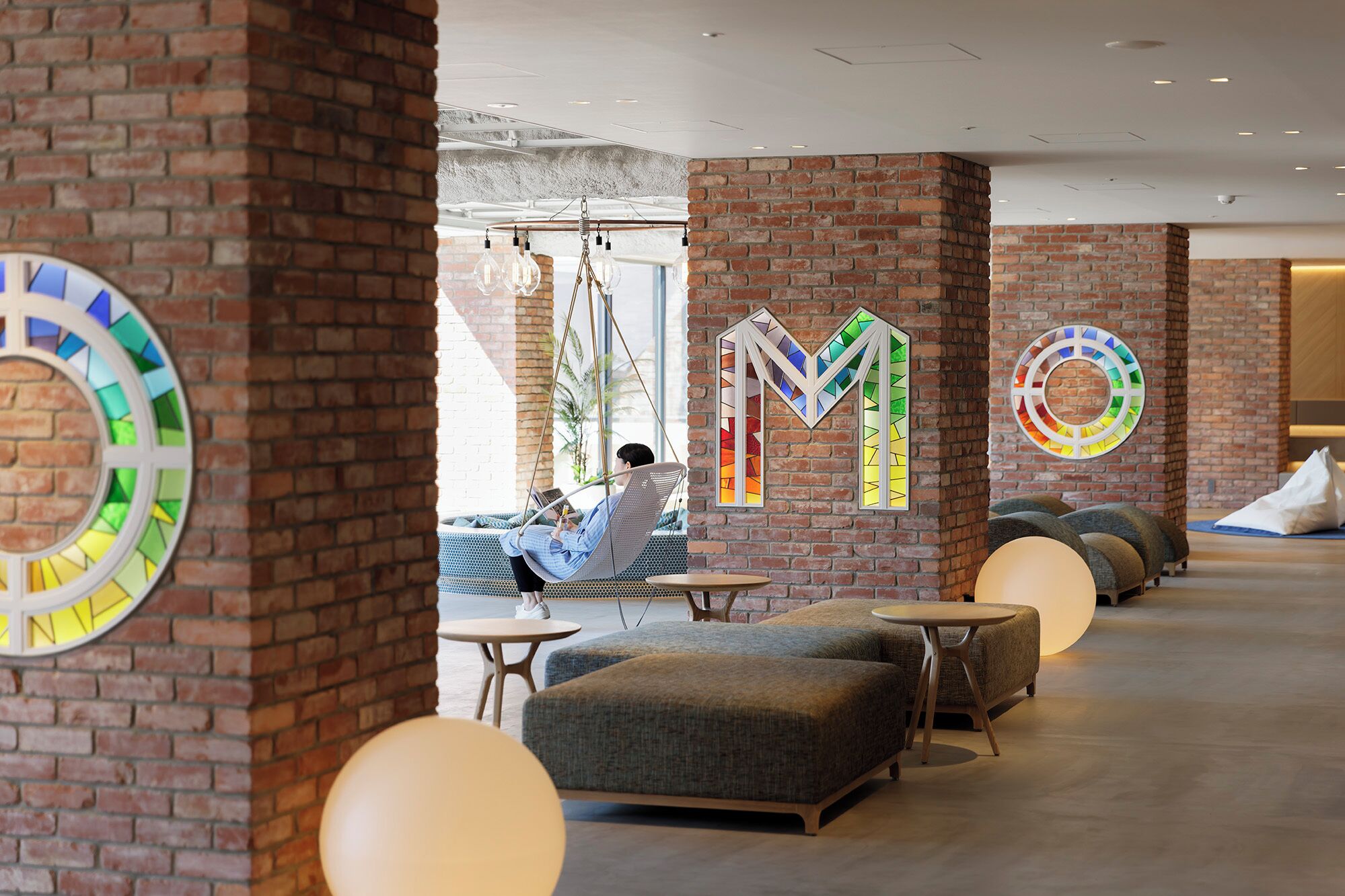 A modern lounge area with brick walls, colorful stained glass letters, and comfortable seating.