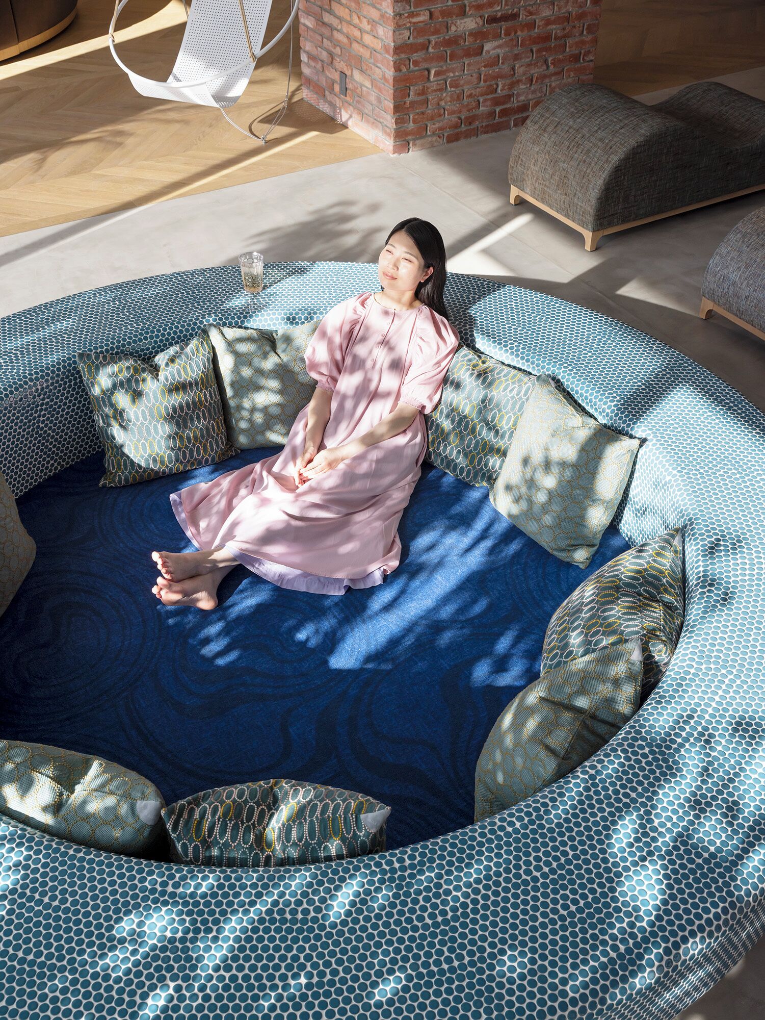 A person sitting on a circular bed with a blue and white patterned bedspread, surrounded by matching pillows.