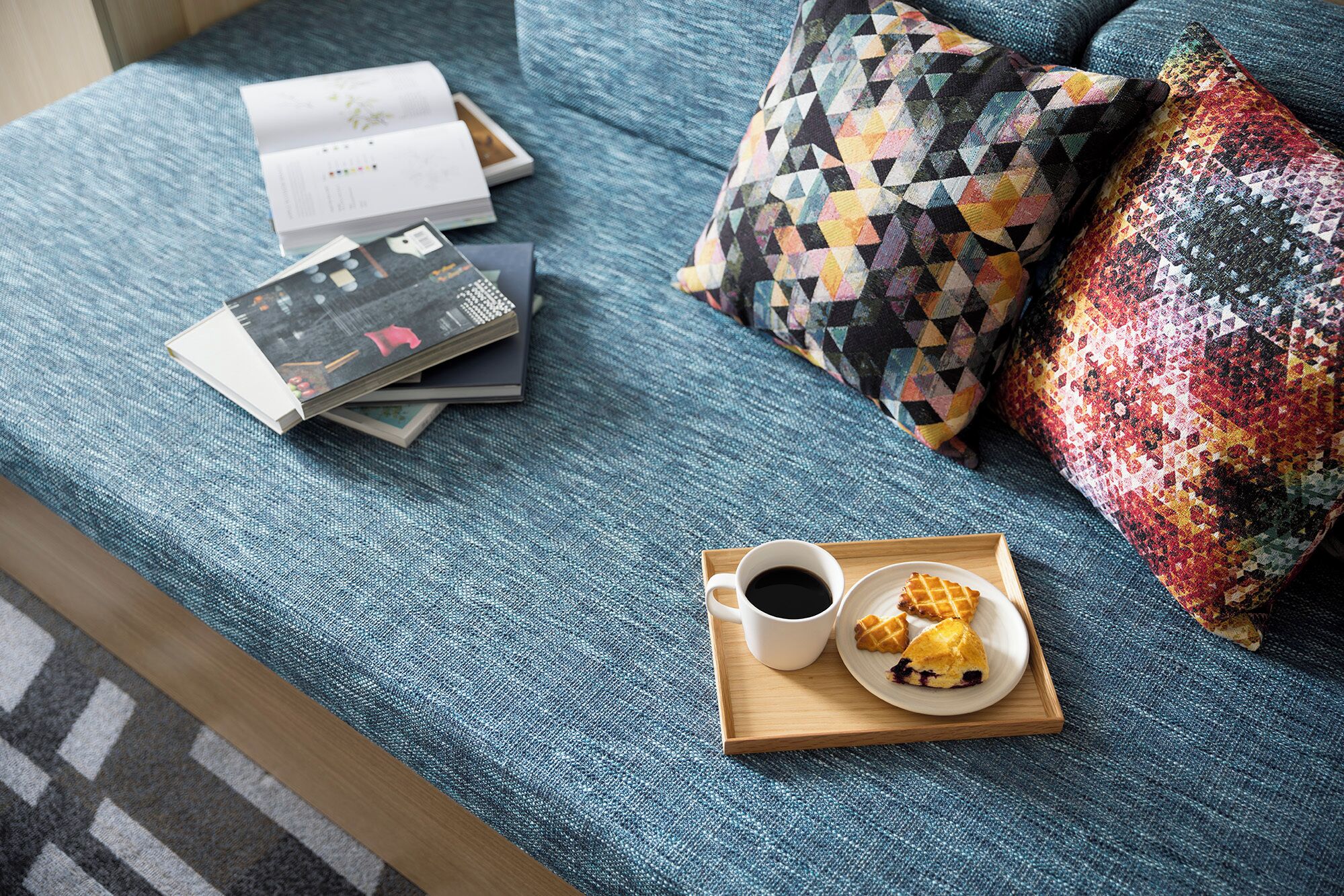 Una cama con una cubierta azul, una bandeja con una taza de café y gofres, y un libro sobre la cama.