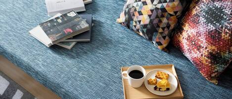 Una cama con una cubierta azul, una bandeja con una taza de café y gofres, y un libro sobre la cama.