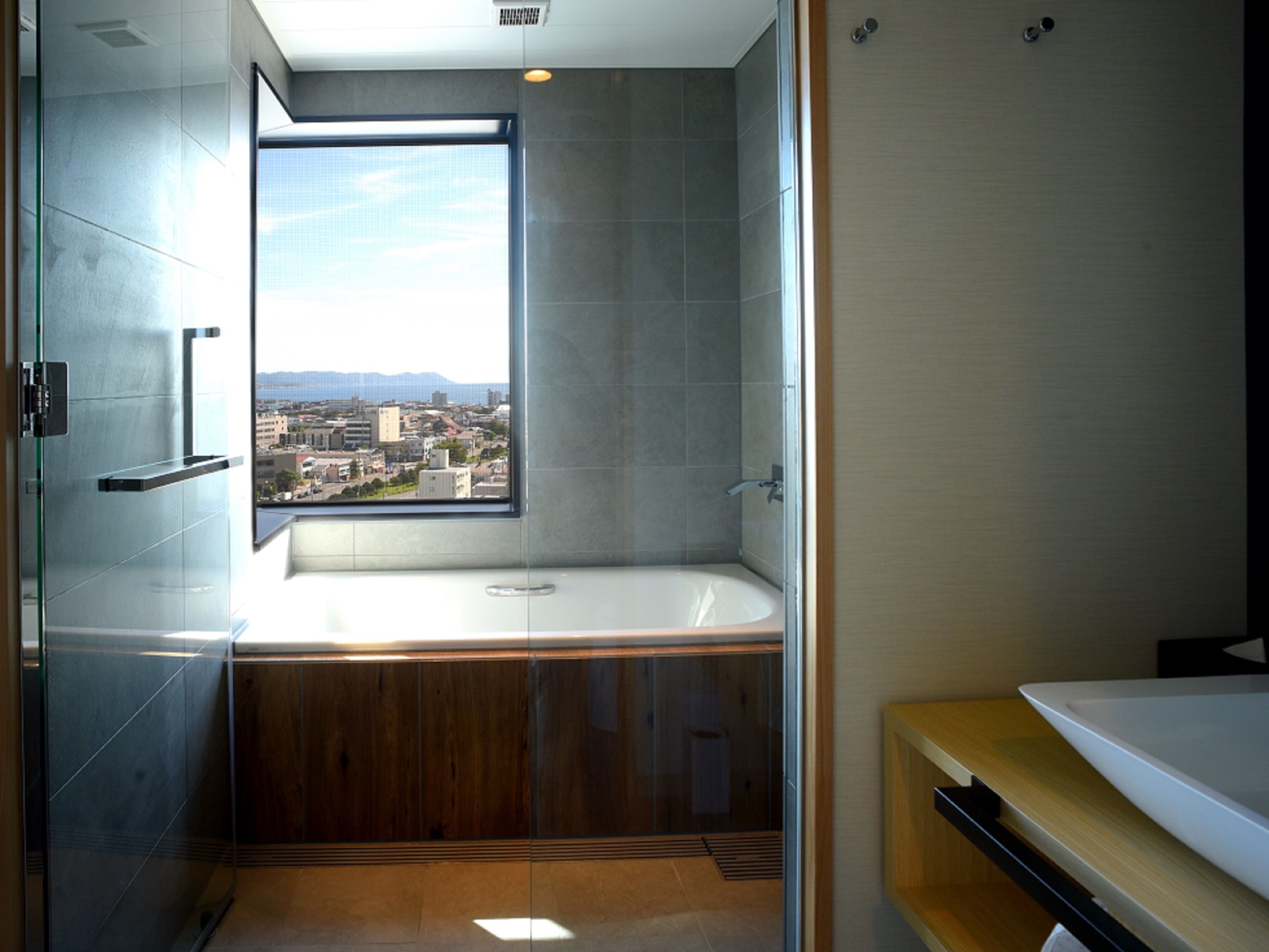 A modern bathroom with a large bathtub, a window offering a city view, and a wooden vanity.