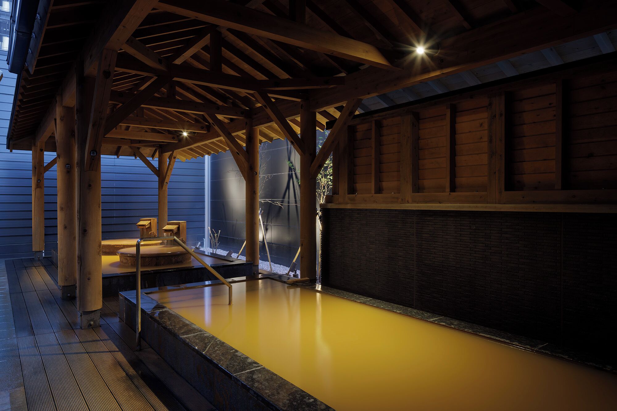 A wooden spa area with a hot tub under a wooden roof structure.