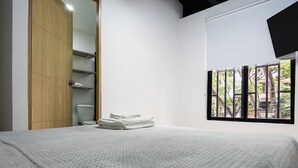 Une chambre à coucher avec un grand lit, une armoire en bois, un placard blanc et une fenêtre donnant sur les arbres.