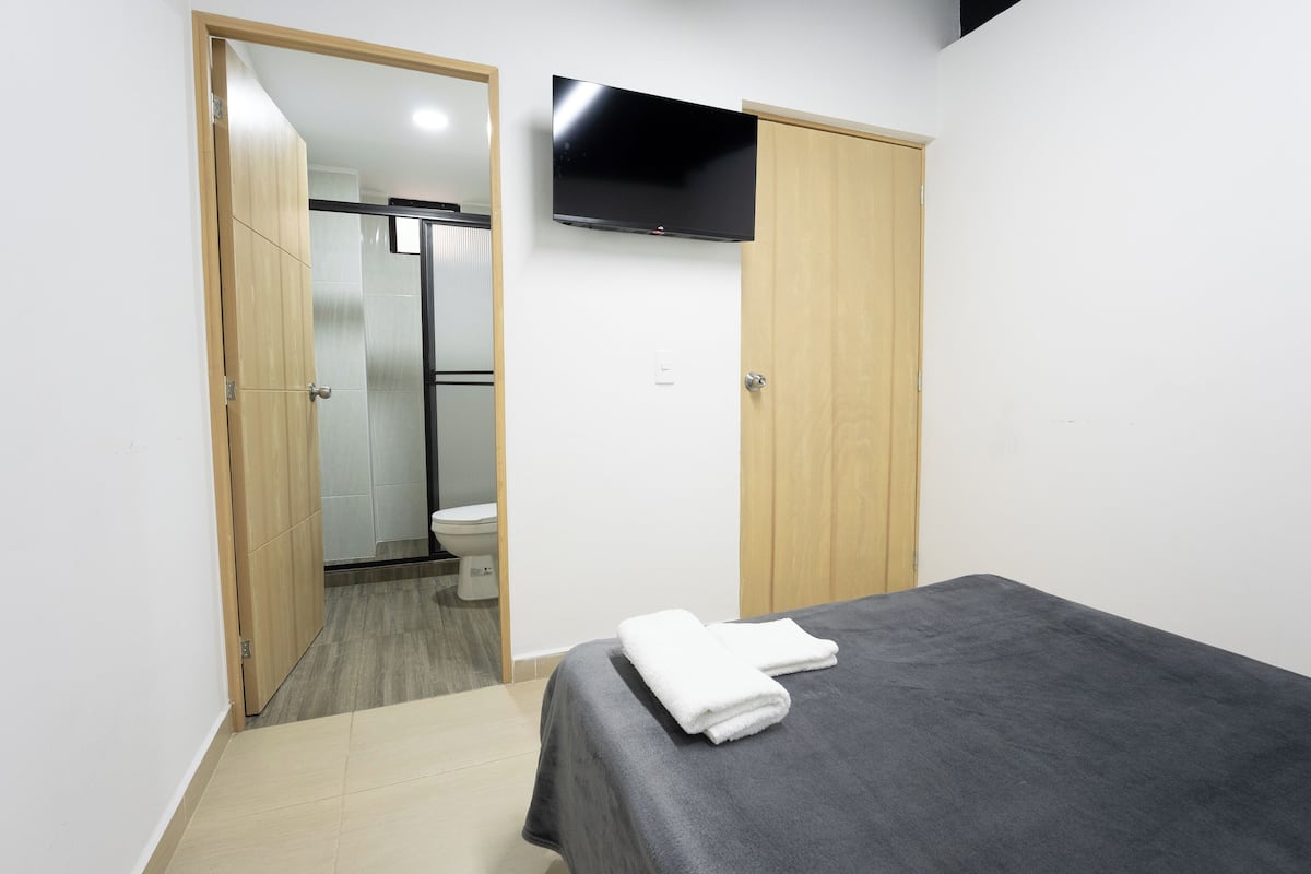 A bedroom with a bed, a TV mounted on the wall, and a wooden wardrobe.