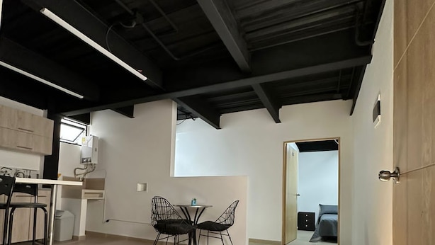 Une pièce spacieuse avec un plafond haut, un coin repas avec une table et des chaises, et une vue sur une autre pièce.