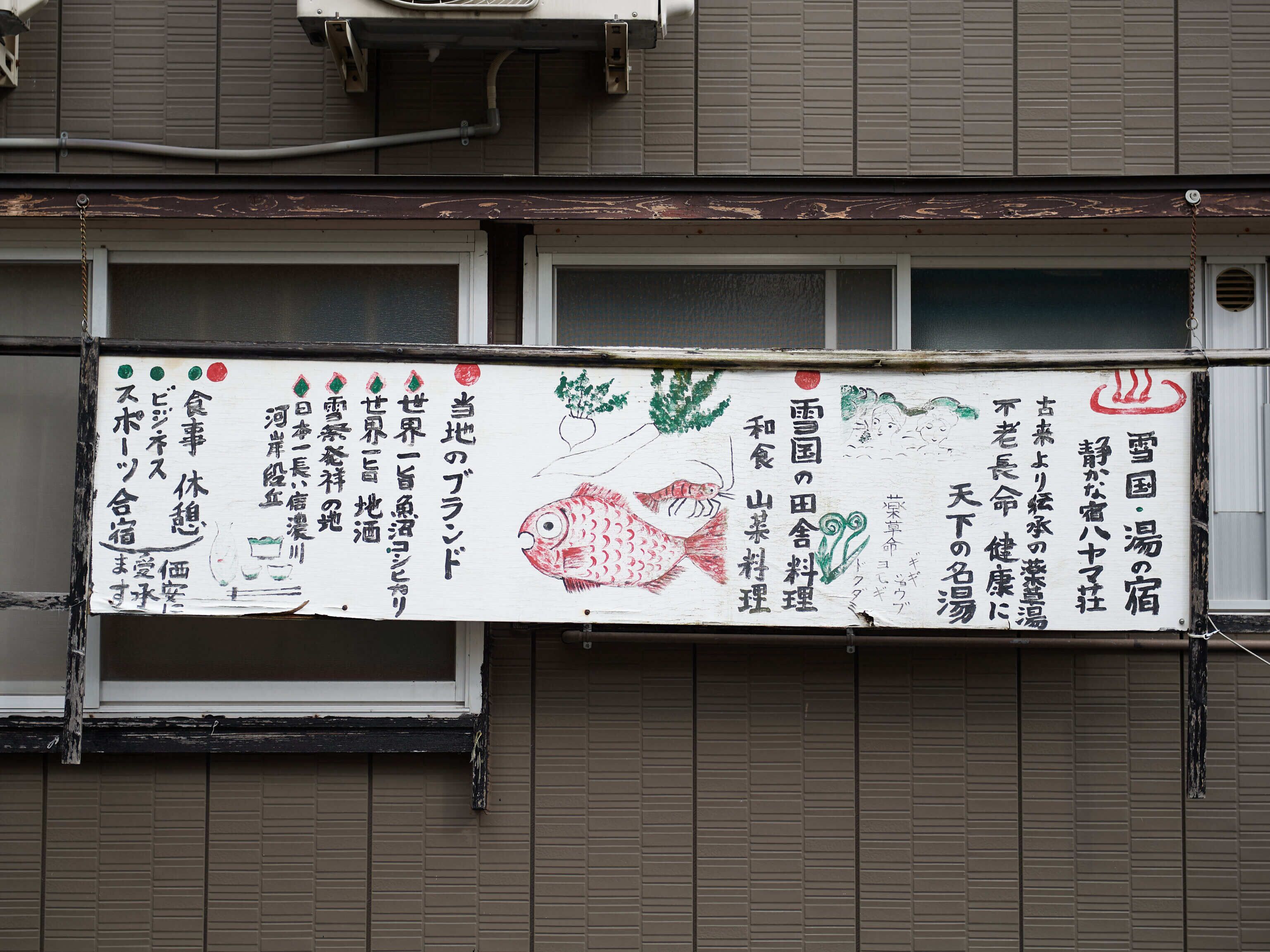 A building with a signboard displaying Japanese text and a fish illustration.