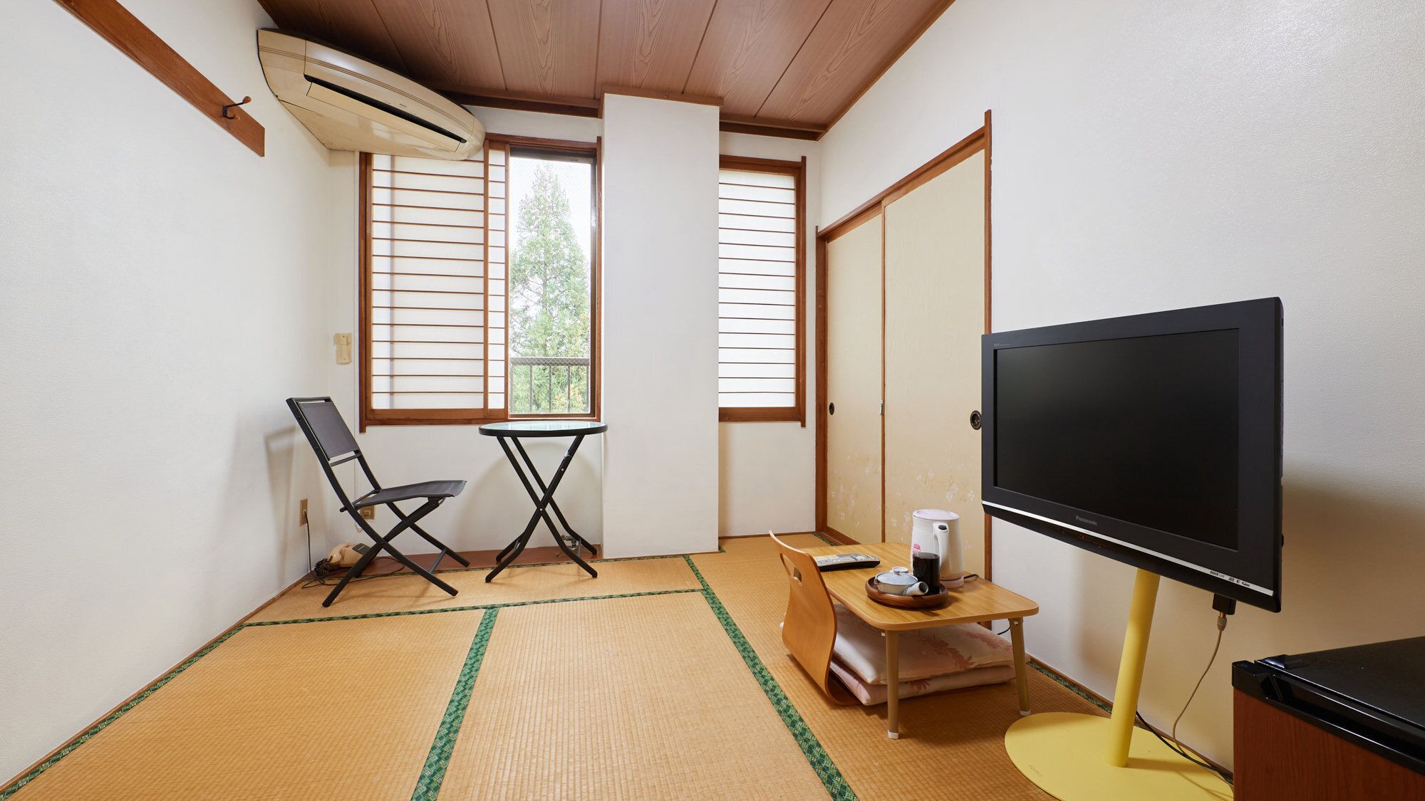 A room with tatami mat flooring, a foldable table, a chair, a television, and a sliding door.