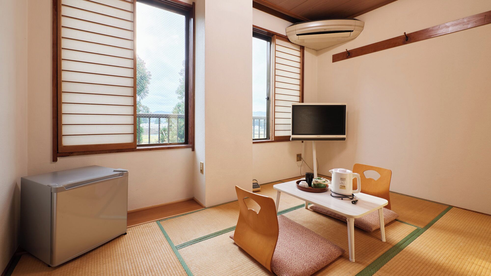 A room with tatami flooring, a television, a small table with a kettle, and a refrigerator.