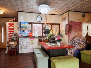 Una habitación pequeña y acogedora, con piso de madera, un banco rojo, una mesita con un reloj y una pared decorada con diversos adornos y letreros.