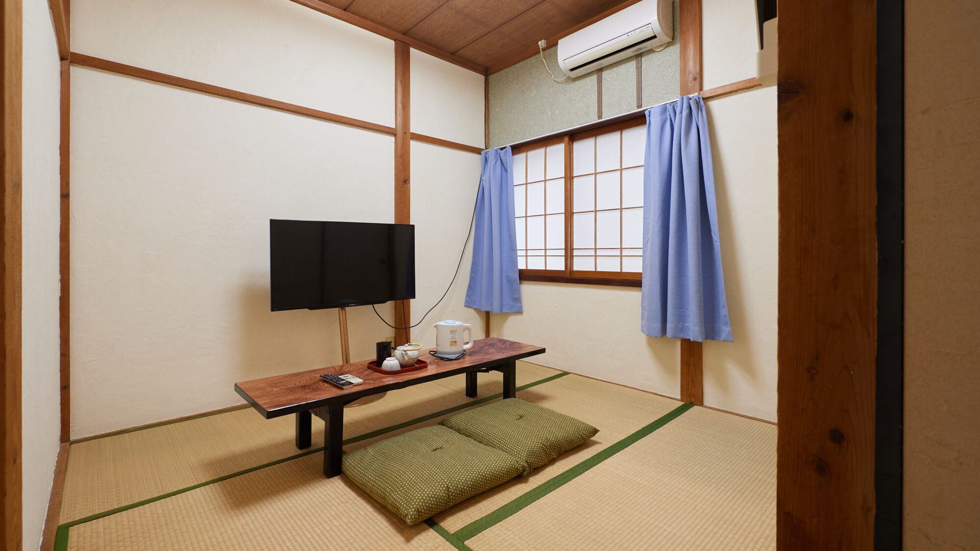A traditional Japanese room with tatami flooring, a television, a kettle, and a futon.