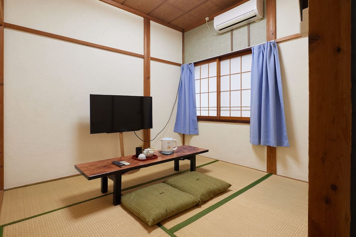 Ett traditionellt japanskt rum med tatamimattor på golvet, en tv, en vattenkokare och en futon.