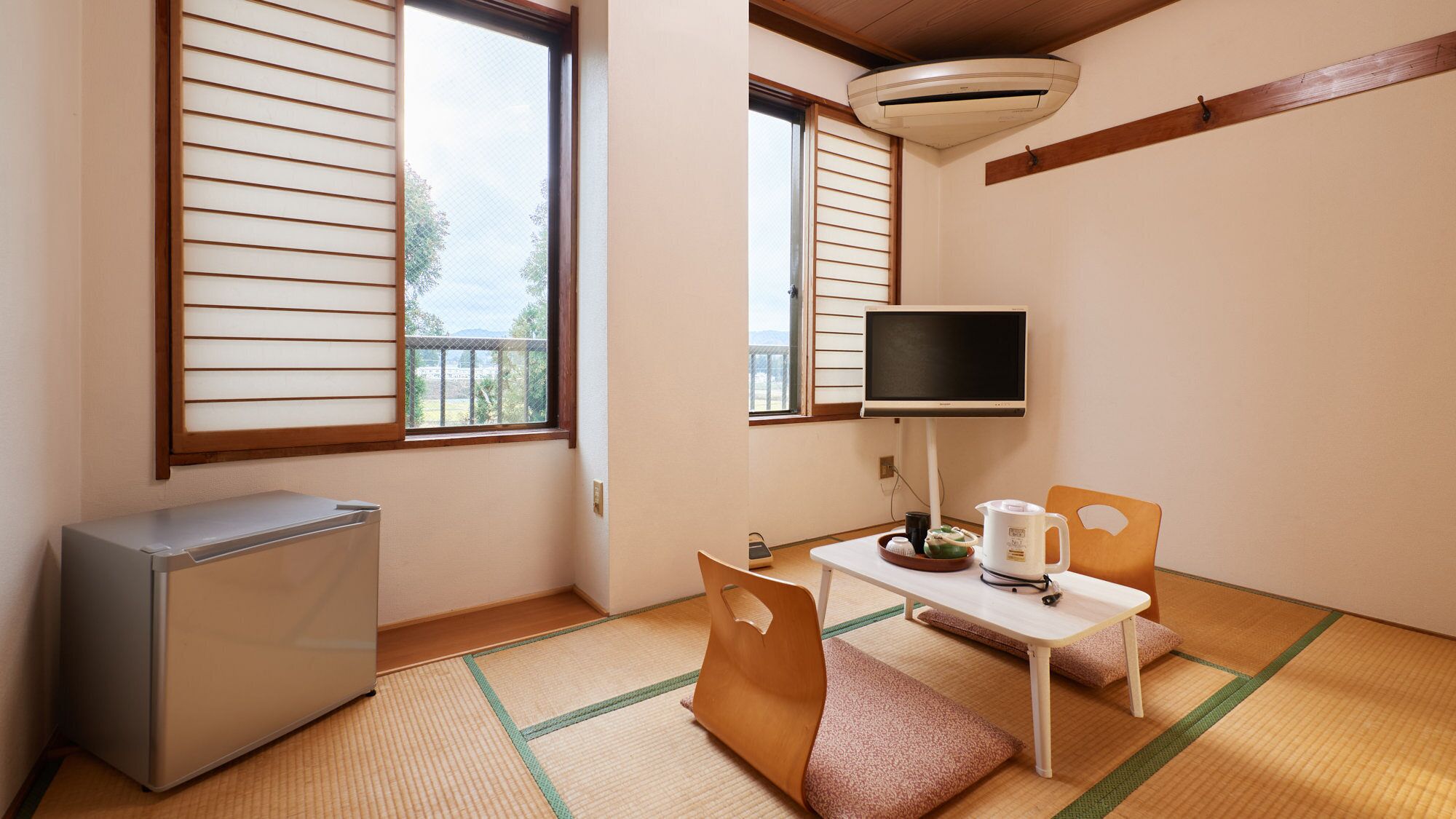 A room with tatami flooring, a television, a refrigerator, and a window with shoji screens.