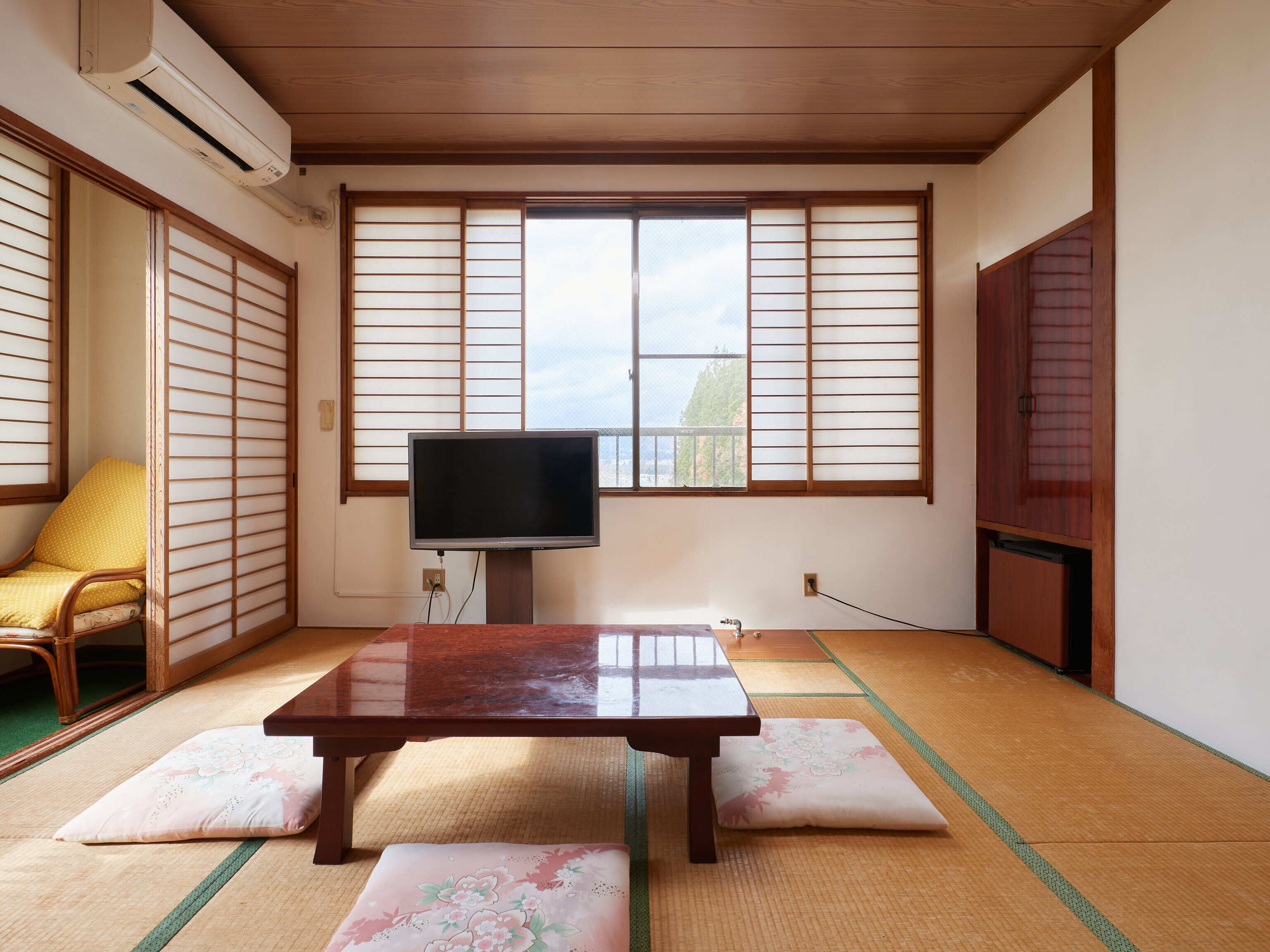 Una habitación tradicional japonesa con suelo de tatami, un televisor sobre un mueble, una mesa de madera y una puerta corredera.