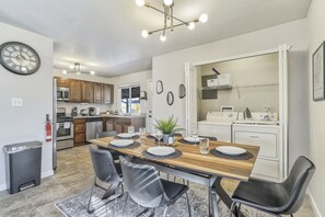 Een moderne keuken met houten kastjes, een inbouwoven en een eethoek met een houten tafel en zwarte stoelen.