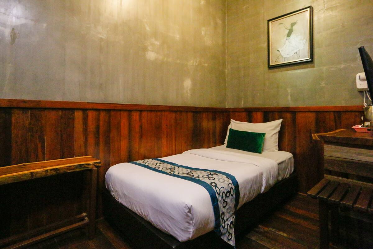 A single bed with a white and blue bedspread, a green pillow, and a wooden headboard.