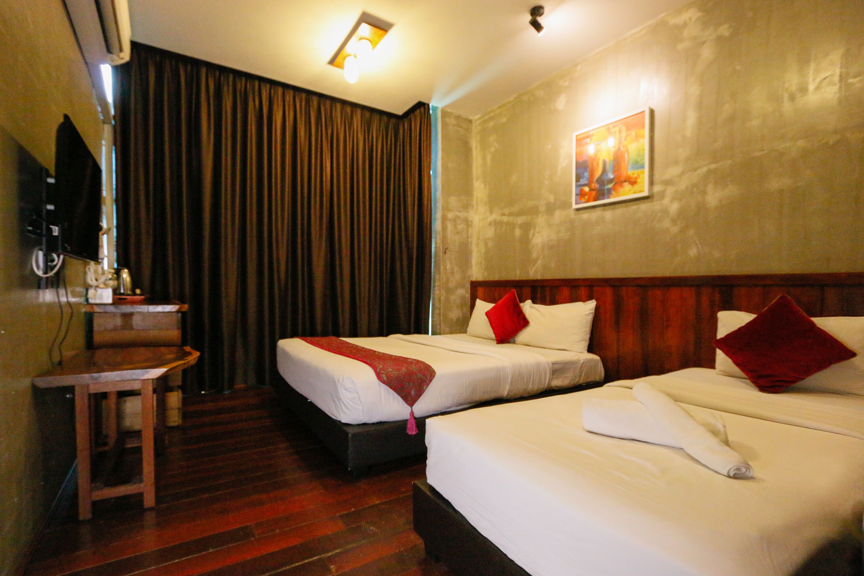 A hotel room with two beds, a wooden desk, a television, and a painting on the wall.