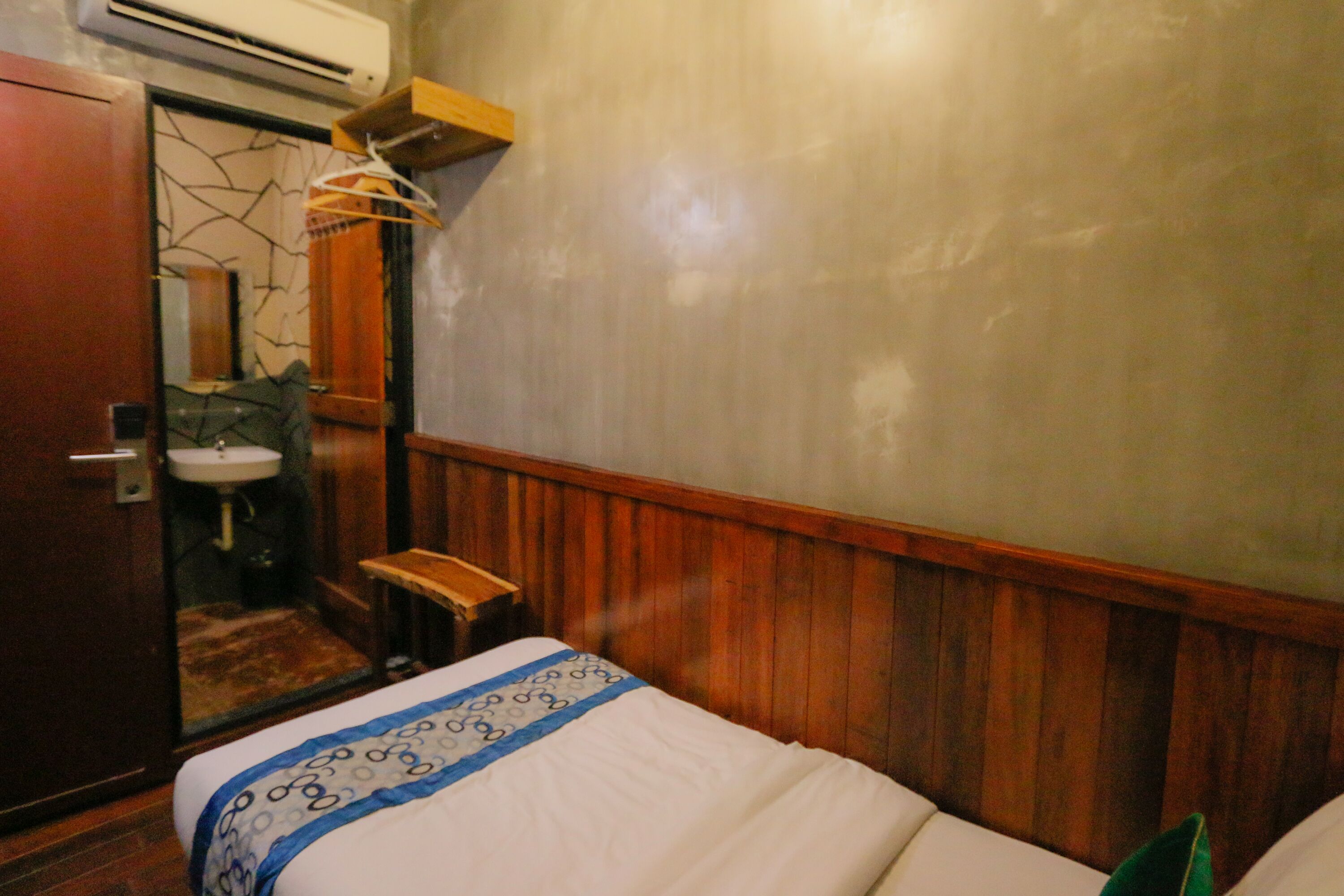 Una habitación de hotel con una cama de madera, un pequeño banco de madera, un lavabo y un espejo.