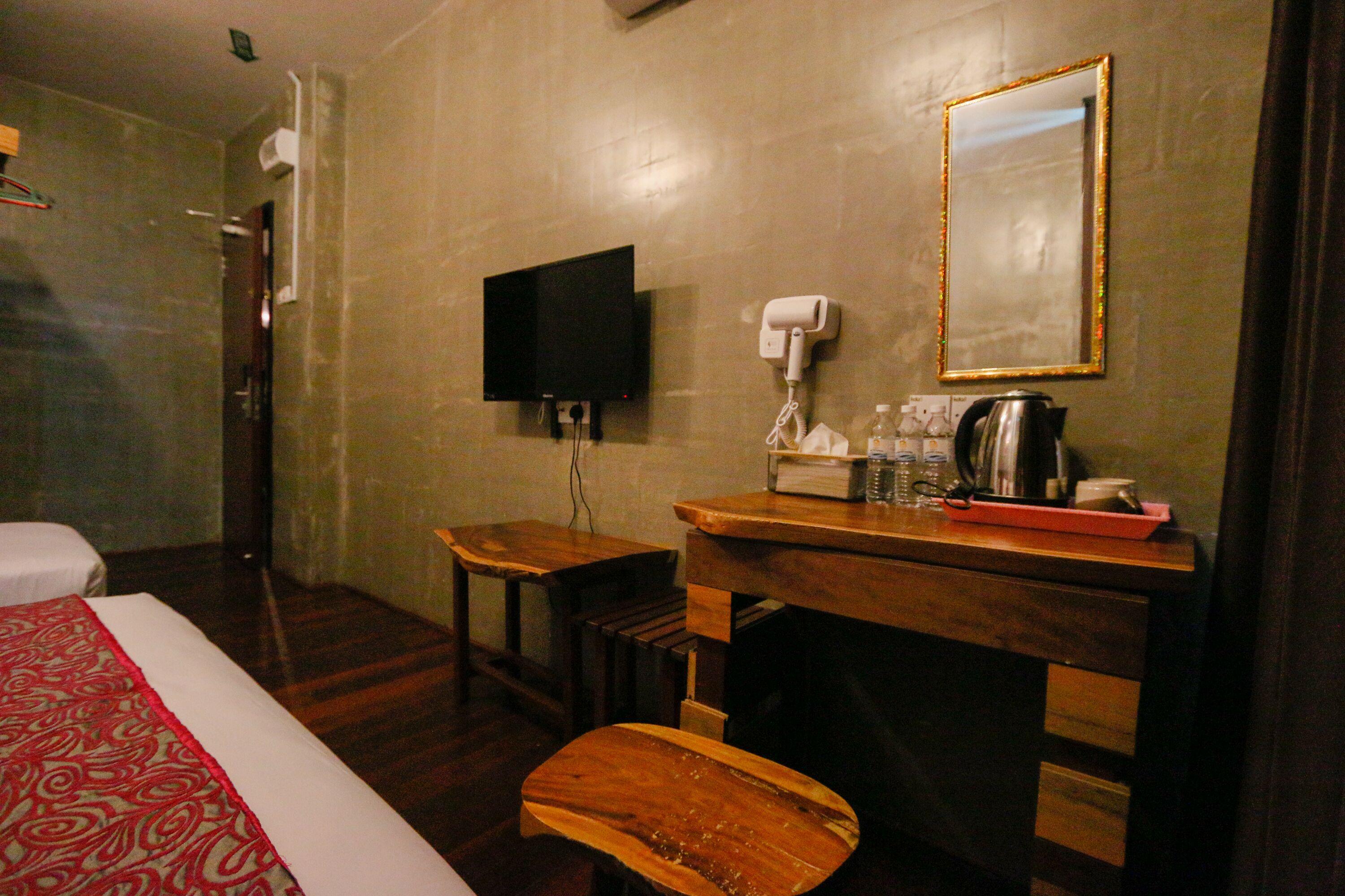 A hotel room with a bed, a wooden desk, a television, a hairdryer, and a mirror.