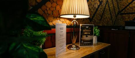 A reception desk with a lamp, a welcome sign, a poster, and a wooden wall with logs.