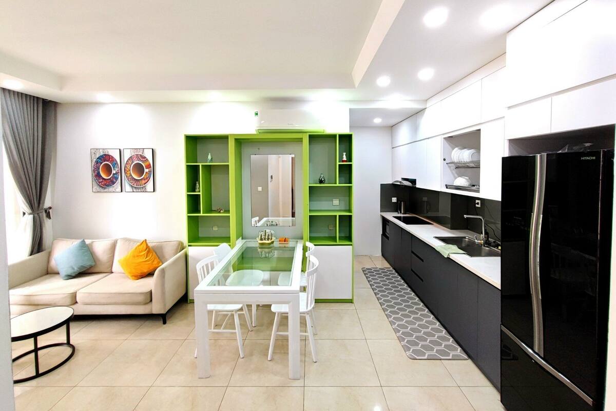 A modern kitchen with a black refrigerator, a dining area with a glass table, and a living room with a sofa and a coffee table.