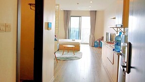 A hotel room with a bed, a small round table, a kitchenette, and a view of the city through large windows. - Vinhomes Dcapital Managed by Anstay Residence (Hanoi)