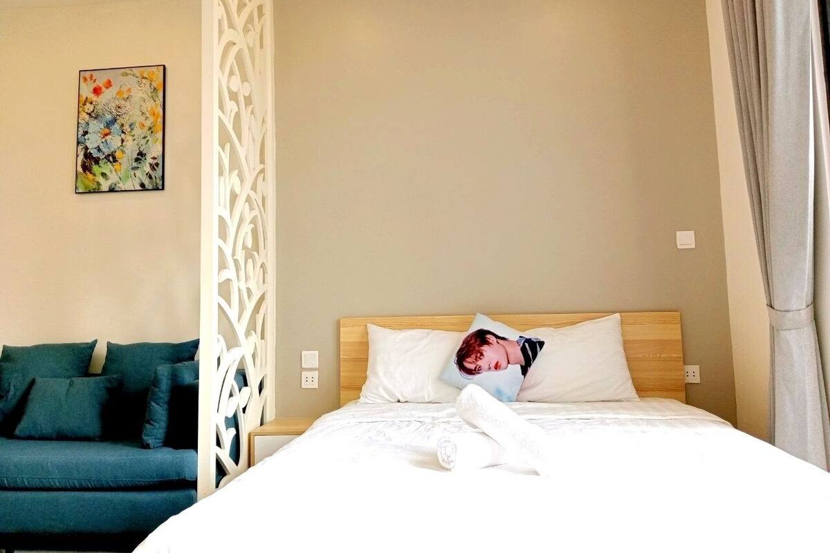 A hotel room with a bed, a decorative partition, a sofa, and a painting on the wall.