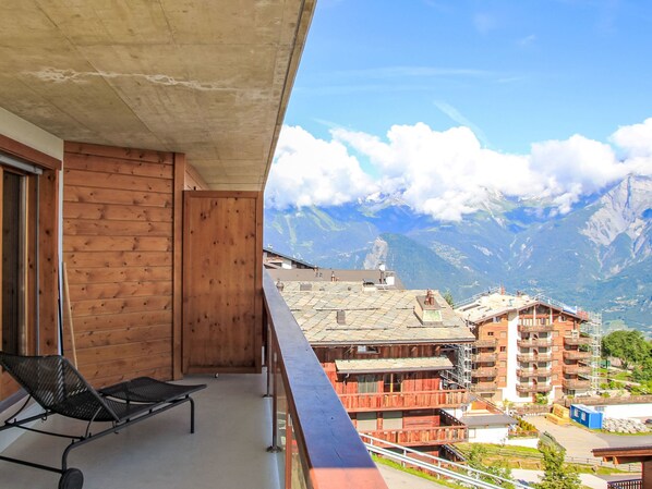 Un balcon avec un mur en bois, une chaise noire et une vue sur les montagnes.