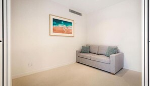 Um quarto com um sofá cinzento, um quadro emoldurado representando uma praia e uma parede branca.
