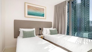 Une chambre d’hôtel avec deux lits, une table de chevet, un tableau encadré au mur et une grande fenêtre donnant sur des immeubles imposants.