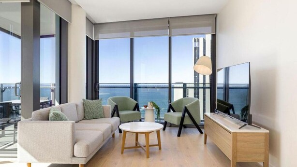Un salon moderne avec un canapé, deux fauteuils, une table basse, un téléviseur et une vue sur l’océan.