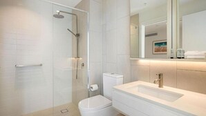 Une salle de bain moderne avec une douche à parois de verre, des toilettes blanches et un meuble-lavabo avec un évier et un miroir.