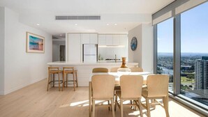 Une cuisine moderne avec des meubles blancs, un îlot central doté de tabourets de bar et une vue sur la ville grâce à de grandes fenêtres.