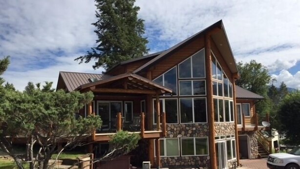 A large, two-story wooden house with a stone foundation, large windows, and a sloped roof. - LAKE VIEW Mountain house w/ HOT TUB
 (Invermere)