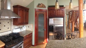 A kitchen with a gas stove, stainless steel refrigerator, wooden cabinets, and a dining area with a table and chairs. - LAKE VIEW Mountain house w/ HOT TUB
 (Invermere)