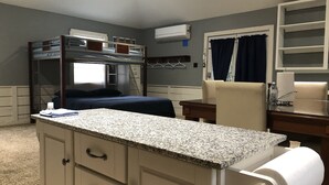 Une chambre avec un lit superposé, un bureau, une chaise et un petit coin cuisine.