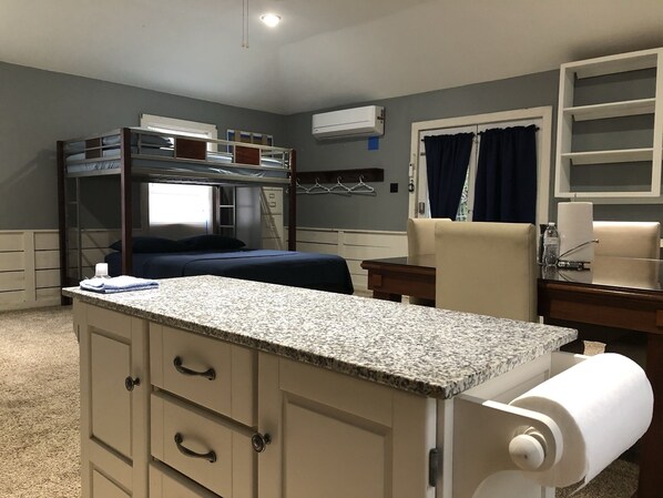 Une chambre avec un lit superposé, un bureau, une chaise et un petit coin cuisine.