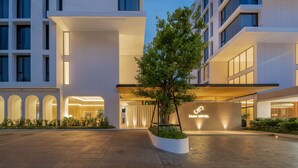 A modern hotel entrance with a well-lit facade, a large tree in the center, and a sign reading "SAAM HOTEL". - Saan Hotel Sathorn (Bangkok)