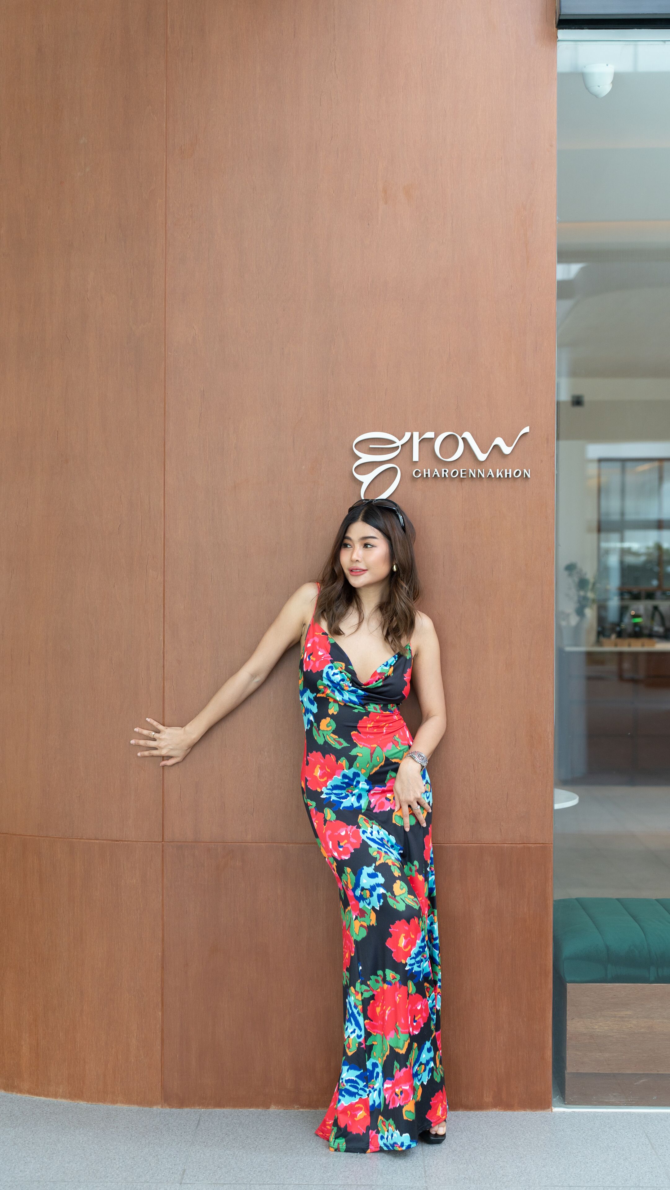 A woman in a floral dress standing against a wooden wall with a logo above her head.