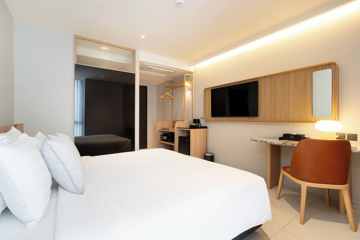 A hotel room with a large bed, a desk with a chair, a television, and a mirror.