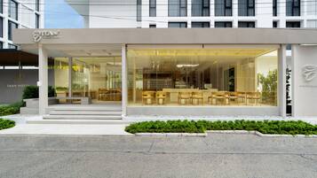 A modern hotel with a glass facade, outdoor seating area, and a visible staircase leading to the entrance.