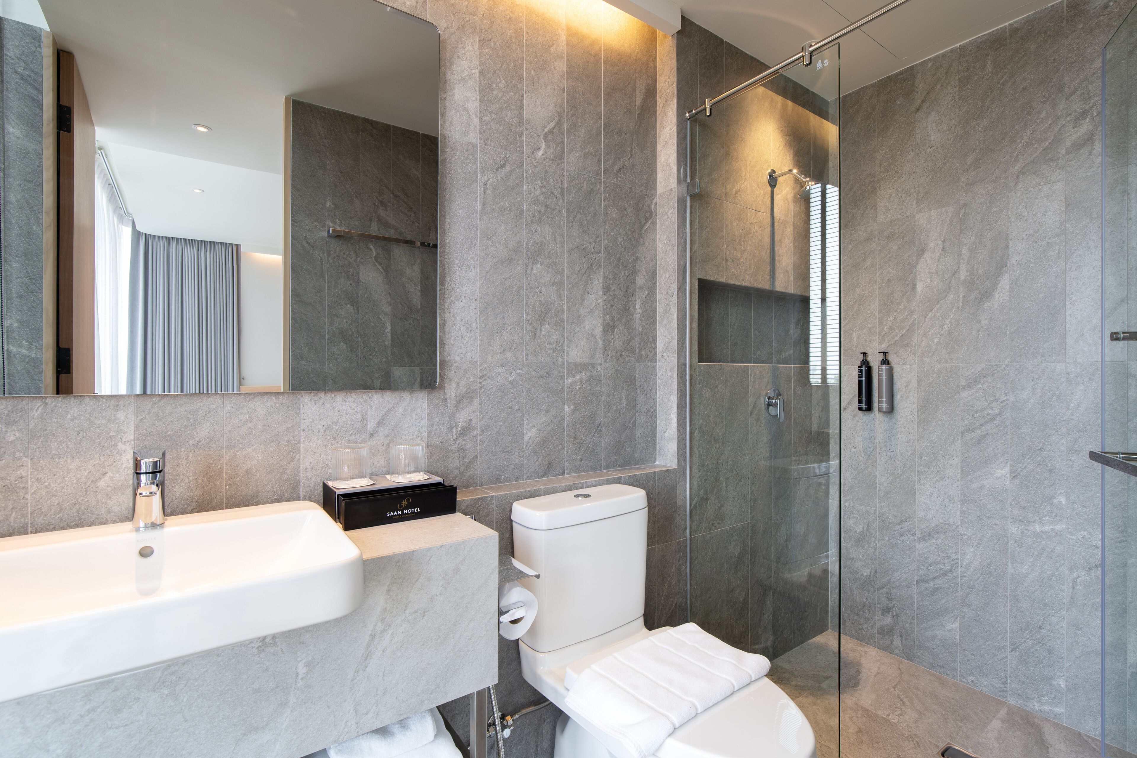Un baño moderno con un espejo grande, un lavamanos, un inodoro y cabina de ducha con mampara de vidrio.