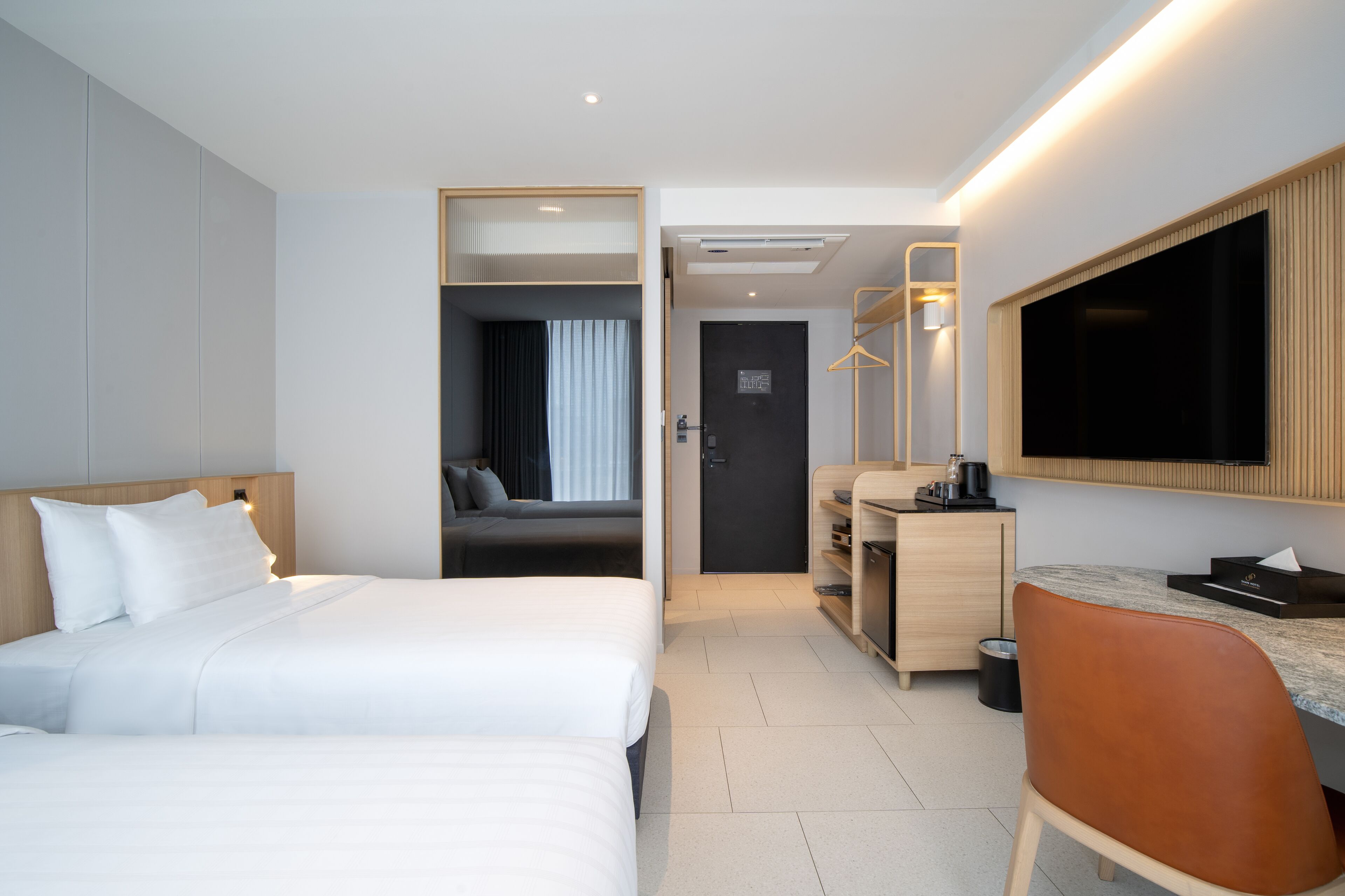 Habitación de hotel con dos camas, un escritorio, un espejo y un televisor.