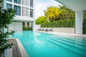 Ein moderner Poolbereich mit klarem, blauem Wasser, Liegestühlen und Blick auf üppiges Grün sowie ein Gebäude mit großen Fenstern.