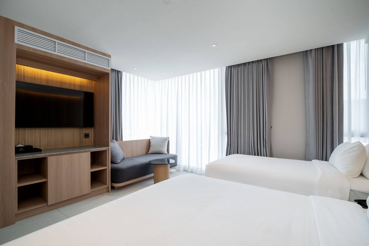 A modern hotel room with two beds, a TV, a sofa, and a built-in wardrobe.