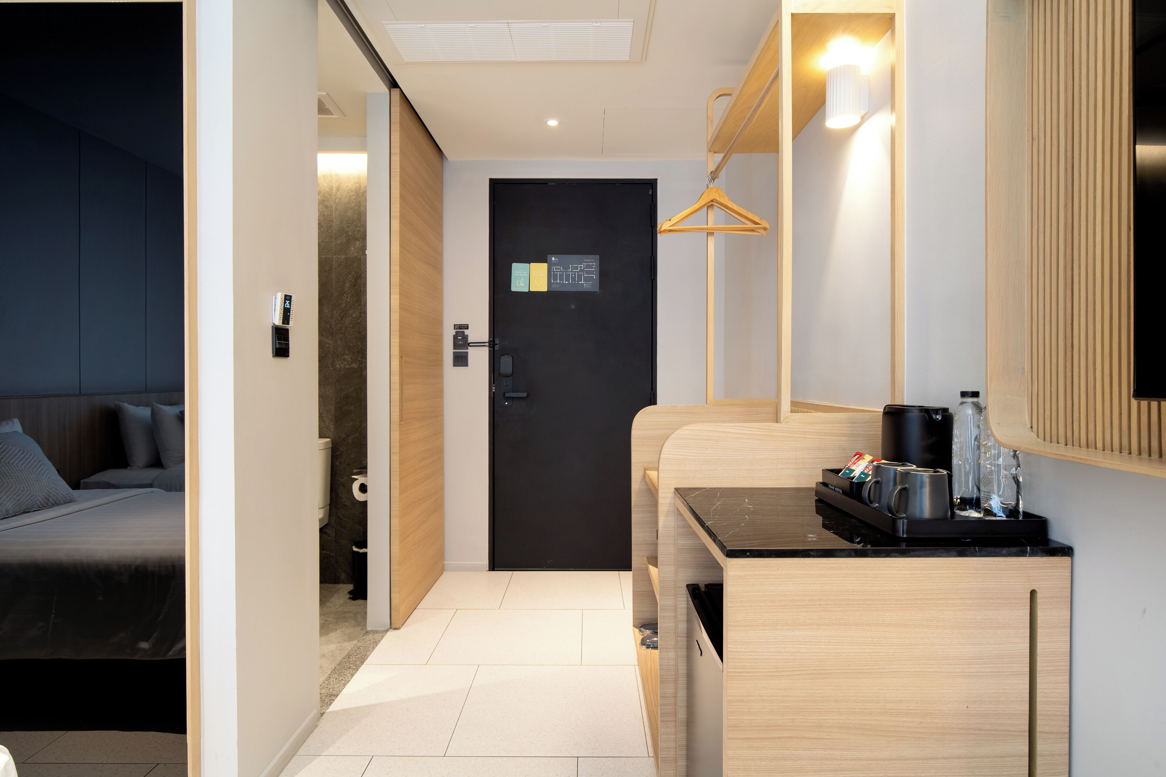 A modern hotel room with a bed, a small kitchenette, a bathroom, and a door with a digital lock.