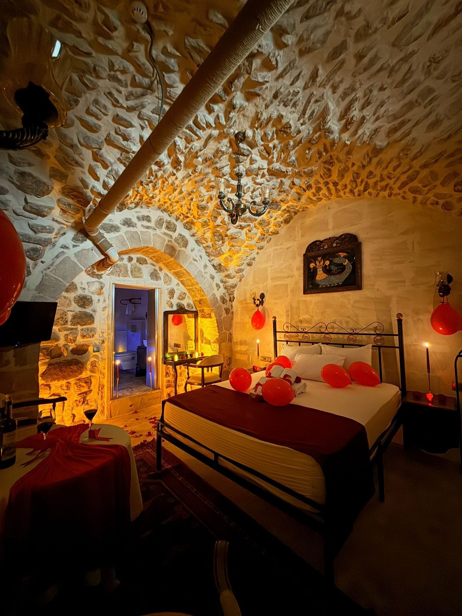 Une pièce aux murs de pierre, avec un lit, un lustre et un coin repas comprenant une table et des chaises.