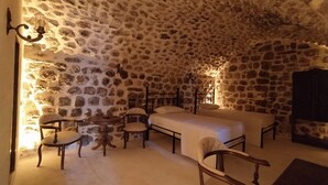 A stone-walled bedroom with a bed, two chairs, a small table, and a wall-mounted lamp. - ARUR KONAGI (Mardin)