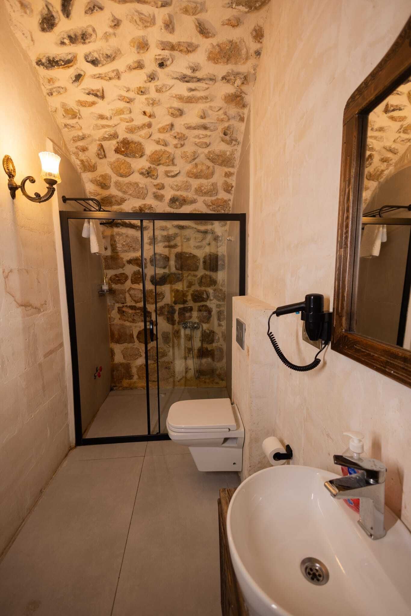Baño con pared de piedra, cabina de ducha de vidrio, lavamanos blanco y espejo.