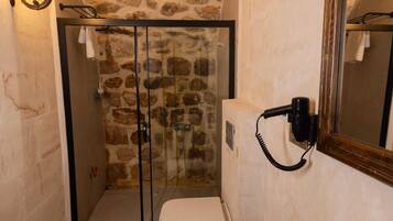 Baño con pared de piedra, cabina de ducha de vidrio, lavamanos blanco y espejo.