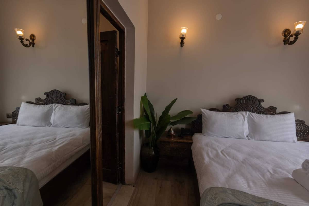 Une chambre d’hôtel avec deux lits, une porte en bois, une plante en pot et des appliques murales.